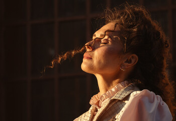 Fototapeta premium Portrait of a woman in vintage clothing, illuminated by warm sunlight, against a backdrop of ancient architecture.