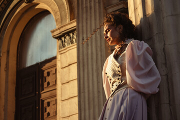 Fototapeta premium Portrait of a woman in vintage clothing, illuminated by warm sunlight, against a backdrop of ancient architecture.