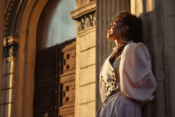 Fototapeta premium Portrait of a woman in vintage clothing, illuminated by warm sunlight, against a backdrop of ancient architecture.
