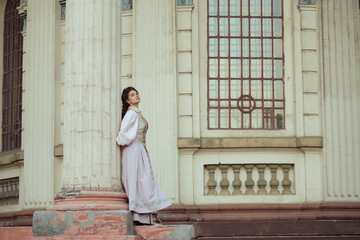 Fototapeta premium An elegant woman in a vintage dress stands by an old stone column