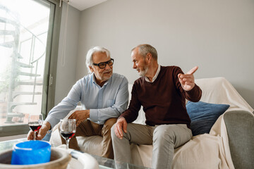 A man points to the side and talks to his male friend who reaches for a glass on the table while...