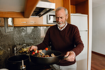 A man shakes a frying pan in which he stirs food
