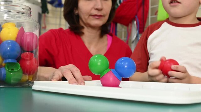 Teacher guiding child during educational activity with colorful construction toys, developing creativity and fine motor skill. Rehabilitation and development of children with autism spectrum disorder
