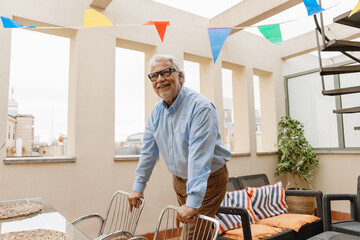 A man stands and leans on a chair with his hands while smiling