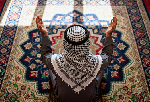 Muslim pray in mosque on prayer rug with hands raised to sky during worship in religious islamic ceremony