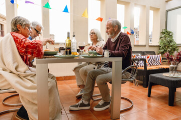 A group of four friends sit at a table with food and drinks while two of them look at the others