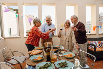 A group of four friends standing at a table and talking while holding glasses