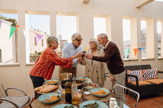 A group of four friends clink glasses and stand at a table while one of them talks