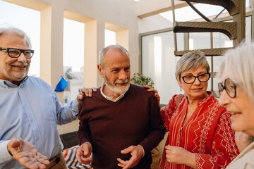 A man and a woman put their hands on the shoulders of the man standing between them while they listen to the woman friend standing next to them
