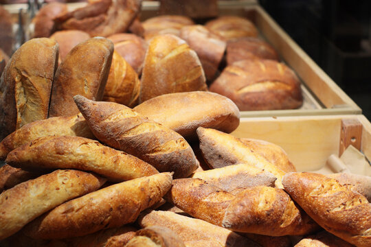 A pile of various fresh loaves of bread in a bakery display. Rustic assortment, golden crusts, artisanal look.