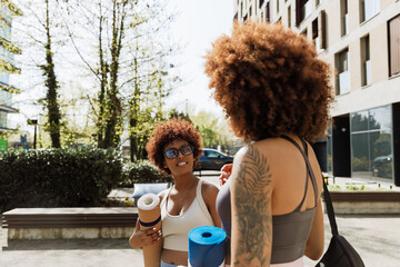 A woman listens to her female friend standing next to her while they hold a mat