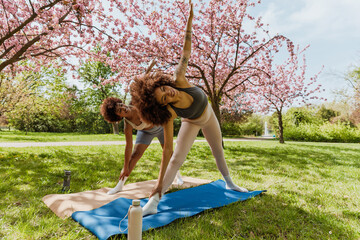 Fototapeta premium Two female friends leaned to the side and raised their arms up while supporting their legs with their other hands and standing on mats