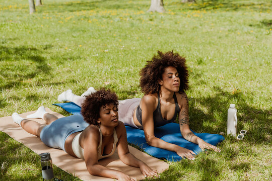Two female friends stretching their backs while lying on mats with eyes closed - Powered by Adobe