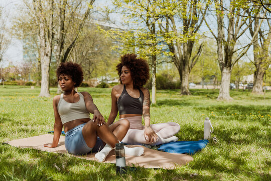 Two female friends stretching and looking away while sitting on mats with legs crossed - Powered by Adobe