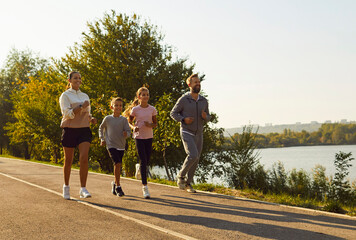 Family with parents and kids running by river. They jog along a riverside park trail at sunrise, smiling in sportswear, keeping an easy pace for fitness. Active family fitness routine outdoors. © Studio Romantic