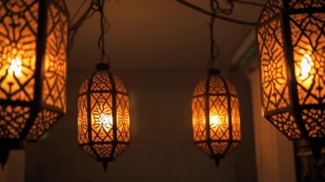 Four antique Moroccan lanterns hang in a row emitting warm orange light illuminating intricate geometric patterns creating a cozy and inviting ambiance perfect for oriental decor or cultural themes