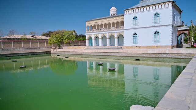View of the green pool and garden at Sitori i Mokhi Khosa in Bukhara, Uzbekistan, with reflections of the historic house.