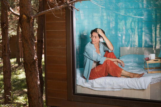 Mindfulness and feel-good moments. middle aged woman rests while sitting on a bed near a window in a country house in the forest. solo retreat