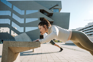 A woman leans her hands on a stone chair and does push-ups with a man next to her