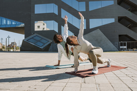 A woman and a man lean on their mats with their hands and reach up while standing and stretching their legs