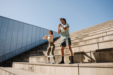 Male and female athletes squatting on stairs while she has elastic bands on her legs