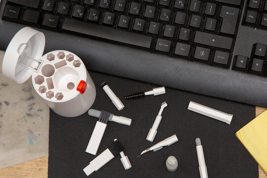 A workspace shows a black keyboard, scattered tools, and a pencil sharpener container. Items include caps, tips, and a yellow notepad. This setup suggests an active work environment.