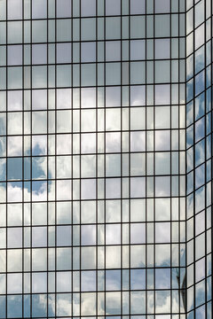 A sleek high-rise building reflects the sky, presenting a visually striking interplay of glass and clouds that symbolizes modern urban life and design.