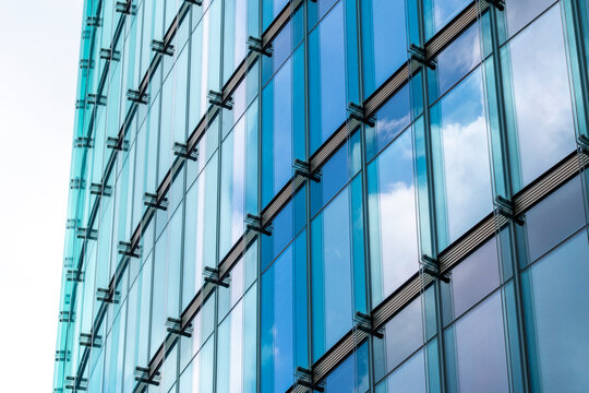 An artistic impression of a glass facade reflecting blue sky and clouds, showcasing the geometric patterns of modern architecture and the harmony of nature and design.