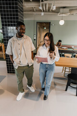 Obraz premium A man and a woman worker walk and read a notebook she is holding and talk while he smiles