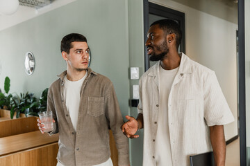 A male worker is holding a glass and listening to a male worker talking to him