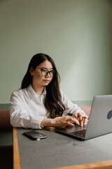 Female worker scrolls through laptop and holds pen while sitting at desk