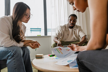 A group of three workers are reading documents held by two of them while they sit at a table