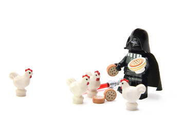 Fototapeta premium Lego minifigure of peaceful Darth Vader from Star Wars is feeding the chicken isolated on white. Editorial illustrative image of stop war concept.