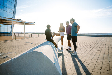 A group of three athletes stand and laugh while listening to a male athlete sitting next to them