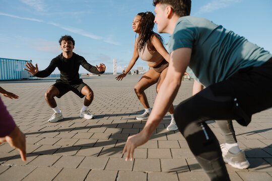 A group of three athletes squat in a circle and hold their arms out to the sides while one of them laughs