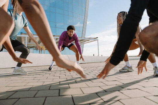 Male athlete standing next to a group of four athletes while they squat and hold their arms down