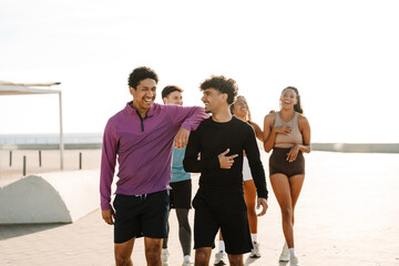 A male athlete rests his hand on the shoulder of another male athlete as a group of three athletes follow them and they laugh