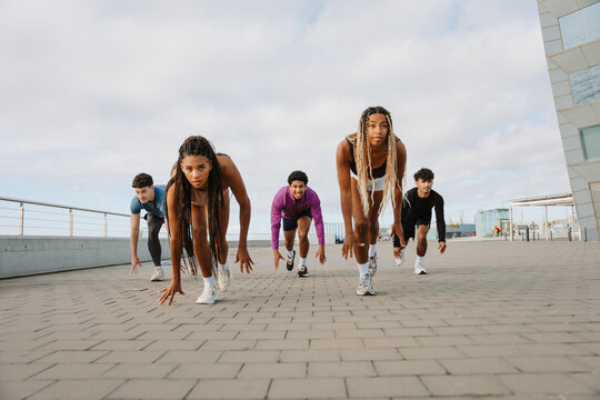 Two female athletes in front of a group of three male athletes as they start running from a starting position - Powered by Adobe
