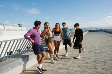 Obraz premium A group of five athletes stand and laugh while two of them lean on the railing and two of them warm up