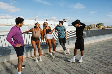A group of five athletes stand and laugh while three of them lean on the fence