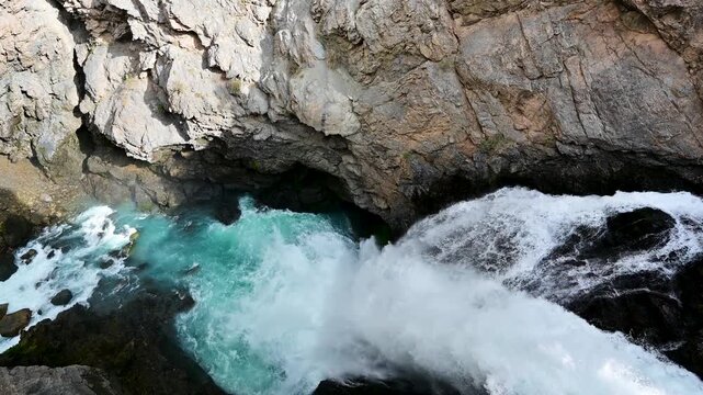 A pan up view from Iskanderdarya Waterfall near Iskanderkul in the Fann Mountains of Tajikistan, revealing rugged alpine peaks and blue sky above a powerful cascade in Central Asia.