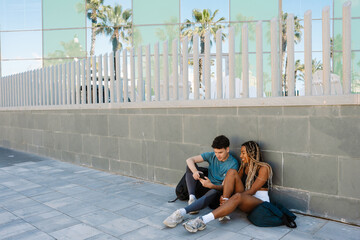 A male athlete is talking to a female athlete sitting next to him on the ground and laughing as...