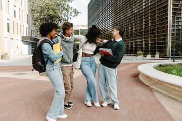 Fototapeta premium A group of four students stand and laugh while hugging and two of them hold notebooks