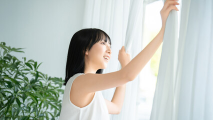 カーテンを開ける若い女性の美容イメージ