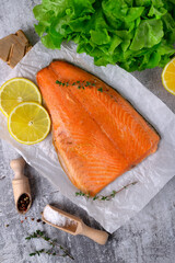Hot smoked trout fillet, lemon slices and thyme on white paper, salt and pepper on grey background. Top view