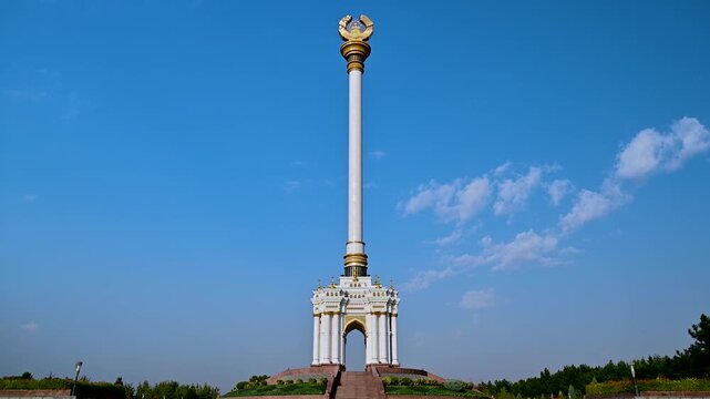 Pan up view of the Independence Monument in Dushanbe, Tajikistan, starting at the base and moving upward to the column against clear blue sky in the capital city.