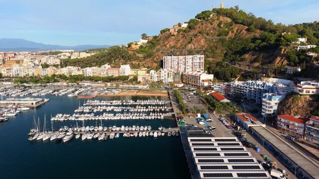 Scenic aerial footage displaying the bustling port of blanes in costa brava, spain, featuring numerous yachts and a building roof covered with solar panels under the morning sun