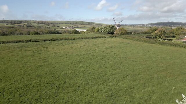 Aerial view of rural landscape with windmill and green fields under blue sky.