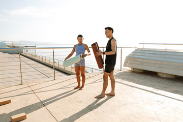 Male and female athletes roll up mats and laugh while standing and talking