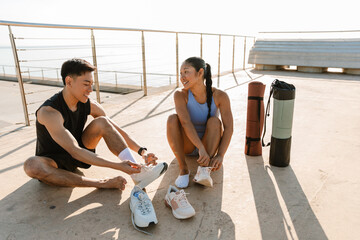 A woman talks to a man while they sit on the ground and laugh while putting on sneakers